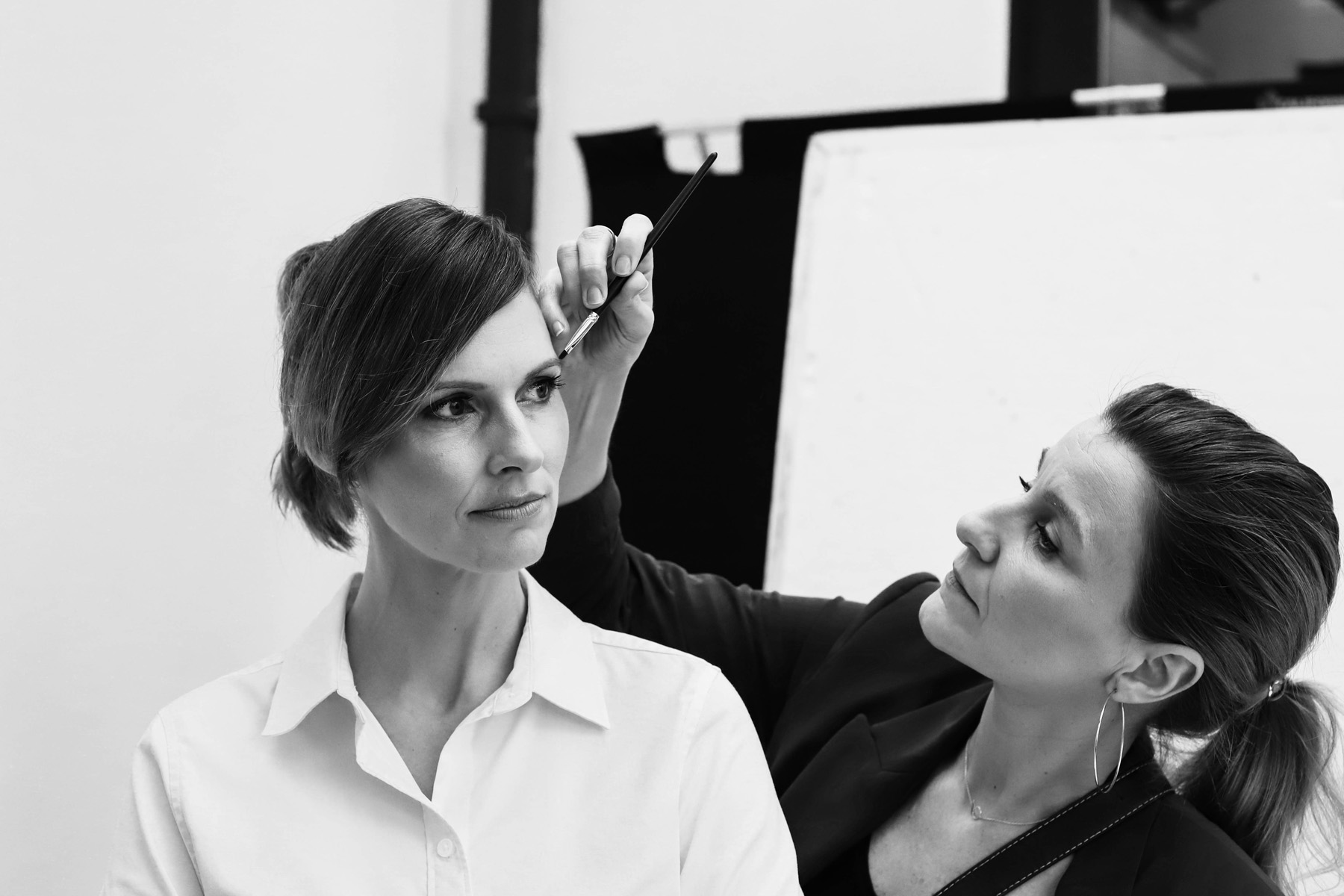 Make-up artist applying make-up to a woman in a white blouse before a photo shoot